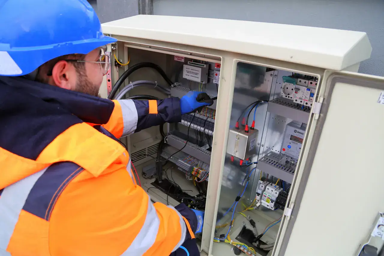 Electrician in a hard hat and high-visibility jacket working inside an open service panel