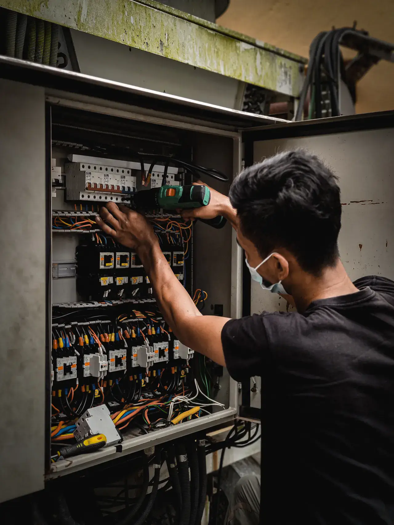 Electrician reaching into an open distribution panel of breakers and control wiring