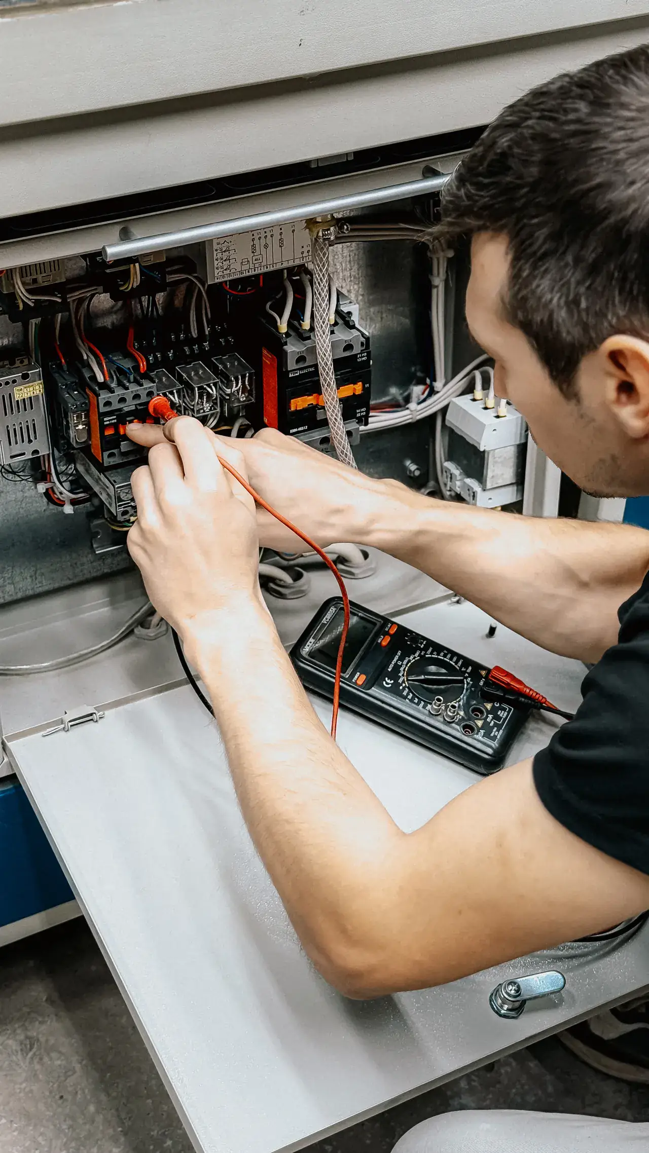 Electrician probing a terminal strip with a multimeter to trace a fault